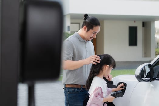 Progressive father and daughter returned from school in electric vehicle that is being charged at home. Electric vehicle driven by renewable clean energy. Home charging station concept for environment