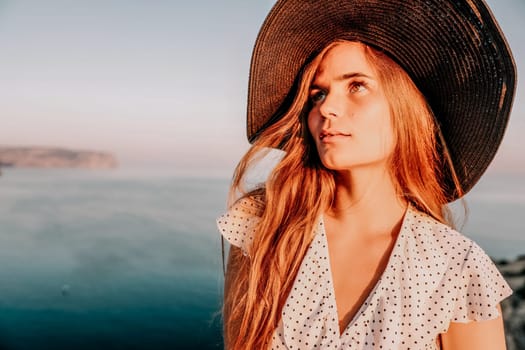 Portrait of happy young woman wearing summer black hat with large brim at beach on sunset. Closeup face of attractive girl with black straw hat. Happy young woman smiling and looking at camera at sea