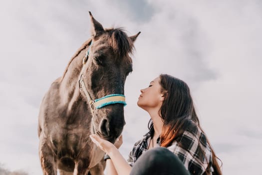 Cute happy young woman with horse. Rider female drives her horse in nature on evening sunset light background. Concept of outdoor riding, sports and recreation.