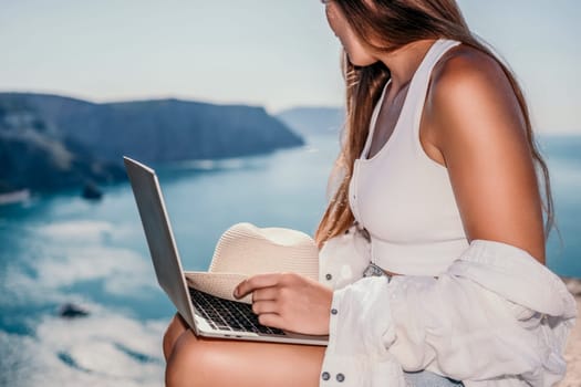 Digital nomad, Business woman working on laptop by the sea. Pretty lady typing on computer by the sea at sunset, makes a business transaction online from a distance. Freelance remote work on vacation