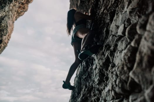 A girl climbs a rock. The athlete trains in nature. Woman overcomes difficult climbing route. Extreme hobby. Tourist woman rock climber hiking on mountains rocks over beautiful sea coast