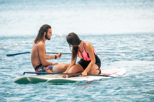 Sea woman and man on sup. Silhouette of happy young woman and man, surfing on SUP board, confident paddling through water surface. Idyllic sunset. Active lifestyle at sea or river