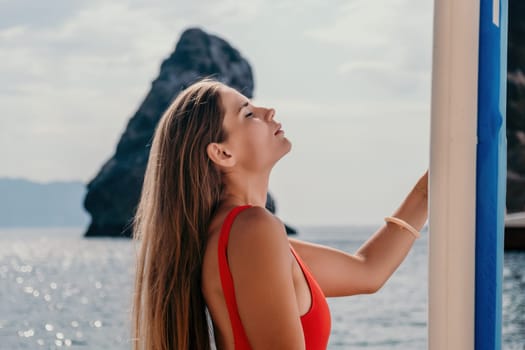 Close up shot of beautiful young caucasian woman with black hair and freckles looking at camera and smiling. Cute woman portrait in a pink bikini posing on a volcanic rock high above the sea