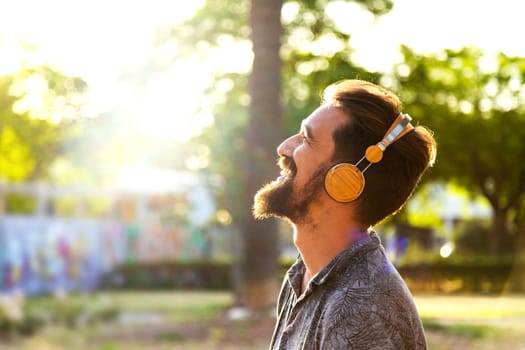 Happy caucasian adult man relaxing listening to music with headphones surrounded by nature. Wellness concept.