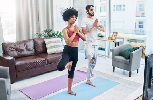 Practising yoga is part of our daily routine. a couple looking at the television while practising yoga at home