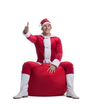 Young man santa claus sit on red bag with presents and smile isolated