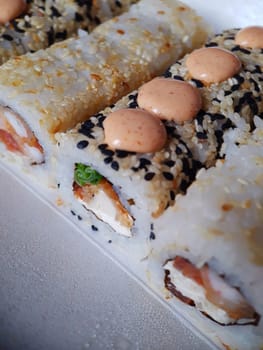 Sushi rolls with fish and cheese, sesame seeds and sauce close-up on the table.