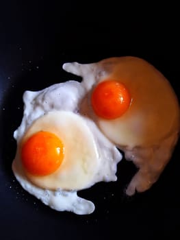 Two fried chicken eggs in a black frying pan close-up. Fried chicken eggs.
