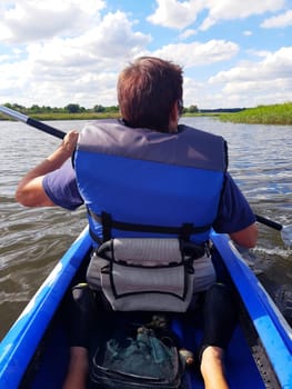 A girl on a blue kayak floats down the river and admires the river landscape.