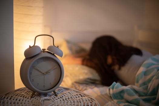 The alarm clock stands on the cabinet next to the bed in which the woman sleeps with the bedside lamp lit. It is already 10 minutes past 10 o'clock on the clock.