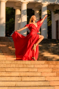 A woman in a long red dress against the backdrop of sunrise, bright golden light of the sun's rays. The concept of femininity, harmony