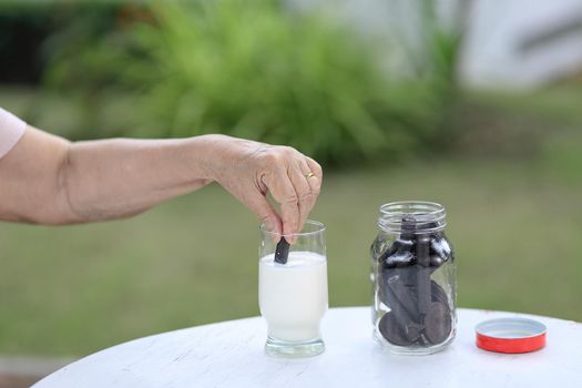 elderly hand dipping a chocolate cookie In milk glass
