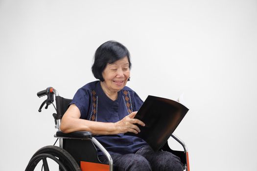 Senior asian woman smiling while reading magazine on white background.