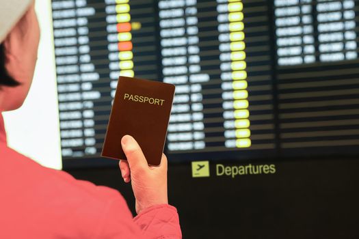 woman in airport  holding passport in her hand ,looking at the flight information board, checking her flight