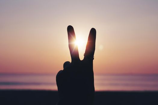 Peace out or fighting metaphor two fingers hand sign in front of a sunset. Happy people enjoying nature. 