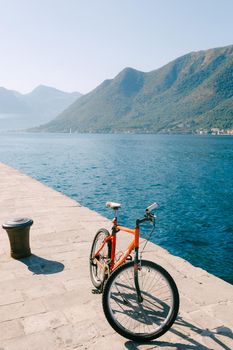 An orange bike on the pier by the river against the green mountains. High quality photo