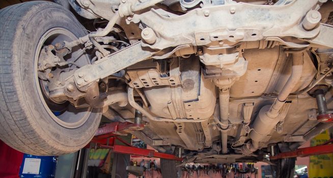 Bottom view of a raised car with worn and rusty parts. In the garage, a person changes the failed parts on the vehicle. Small business concept, car repair and maintenance service.