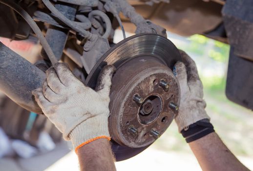 The man's hands remove the worn brake disc from the rear wheel hub. In the garage, a person changes the failed parts on the vehicle. Small business concept, car repair and maintenance service.