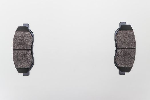 Two brake pads on the edges of the table, parts for car repair. A set of spare parts for servicing the braking system of a vehicle. Details on white background, copy space available.