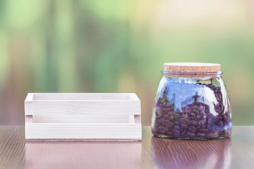 Coffee beans in a glass jar with a wooden crate on a wooden table.