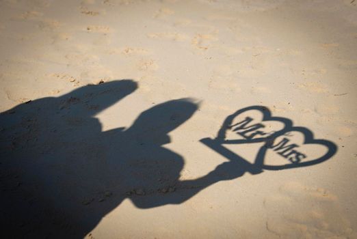 Abstract silhouette shadow on sandy beach of couple holding mr and mrs sign on wedding day