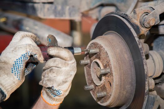 Hands loosen the bolt of the worn and rusty rear brake disc. In the garage, a person changes the failed parts on the vehicle. Small business concept, car repair and maintenance service.