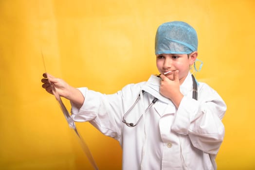 Smiling child boy doctor on yellow background. Male doc in white medical gown. Healthcare health medicine concept. Mock up copy space