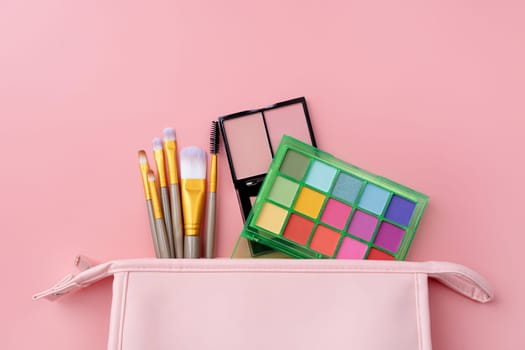 Bright summer eyeshadow palette and makeup products in pink cosmetic bag on pink background. Makeup cosmetics. Colorful colors. Place for text. Flat lay. Top view. layout