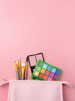 Bright summer eyeshadow palette and makeup products in pink cosmetic bag on pink background. Makeup cosmetics. Colorful colors. Place for text. Flat lay. Top view. layout