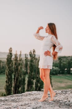 Romantic beautiful bride in white dress posing with sea and mountains in background. Stylish bride standing back on beautiful landscape of sea and mountains on sunset