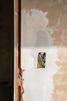 a bundle of multi-colored tangled wires in a hole in a peeling wall in an apartment being renovated. High quality photo