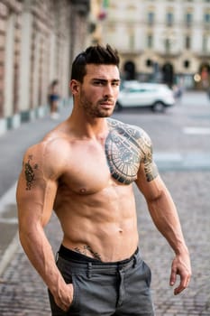 Handsome muscular shirtless man with tattoo posing in European city center, Turin, Italy. Tattoo reads: We are free to start again, in Italian