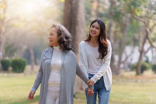 Adult daughter holding her elderly mother hand with love and walk together.