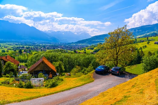 SWITZERLAND, ST GALLEN - MAI 2017: Toyota Avensis T25 and brocken car on the road near wooden cottage houses on green fields, Grabs, Werdenberg, St. Gallen Switzerland.