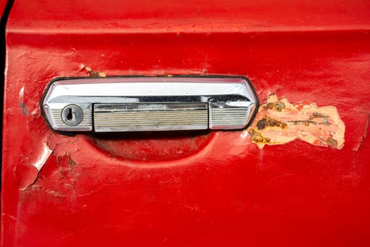 old car door handle close-up. The red door of an old car with a keyhole and peeling paint and putty