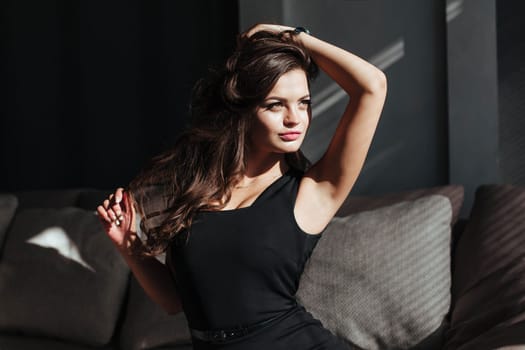 a girl in a black dress sits on the couch and looks out the window.