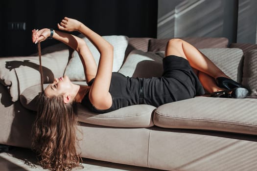 beautiful woman in black dress lies on the sofa and touches her hair.
