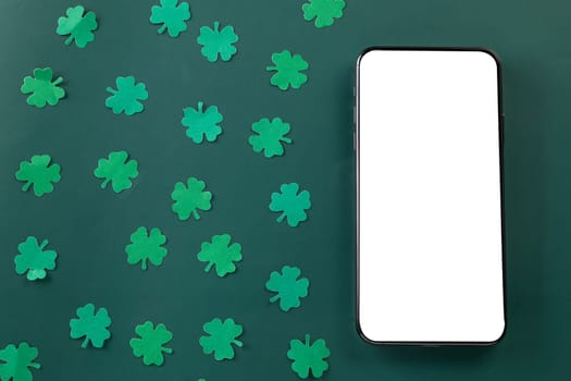 St Patricks Day. overhead flat lay of paper cut clover leaves festive decor and mobile phone blank screen, shamrocks leaf with smartphone holiday symbol on colour background, Banner greeting card