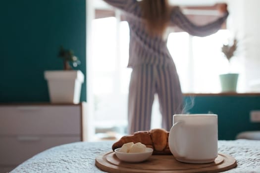 croissant and coffee in the foreground on the back of a girl in pyjamas. breakfast concept