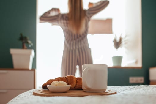 croissant and coffee in the foreground on the back of a girl in pajamas. breakfast concept