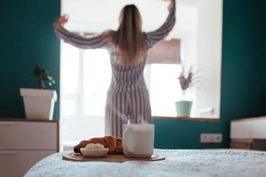 croissant and coffee in the foreground on the back of a girl in pyjamas. breakfast concept