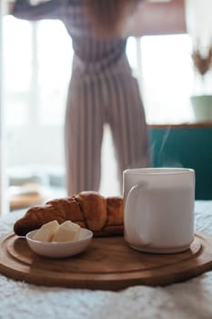 croissant and coffee in the foreground on the back of a girl in pyjamas. breakfast concept