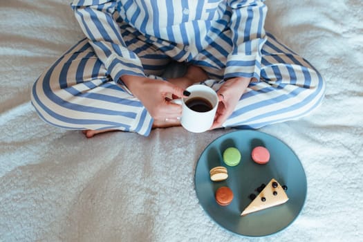 a woman in the morning drinks coffee and eats sweets cheesecake sweet macaroni . breakfast in bed concept