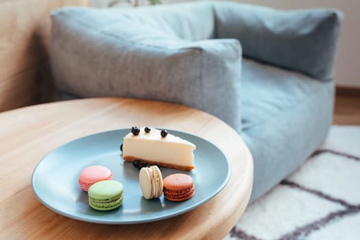 a cheese cake with blackcurrant and macarons on a turquoise plate sits on the edge of the coffee table. sweet breakfast concept
