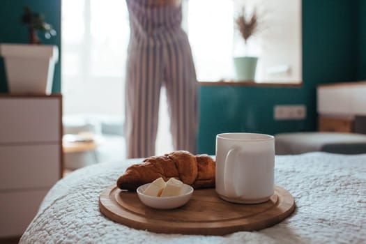 croissant and coffee in the foreground on the back of a girl in pyjamas. breakfast concept