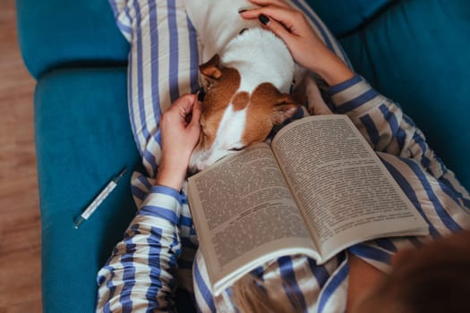 sick ginseng in pajamas is lying on the couch with a thermometer and on her feet is the dog jack rusl. pet health and care concept.