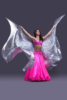 Full length portrait of beautiful dancer performing oriental dance with silver wings