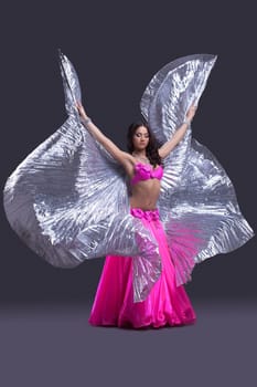 Full length portrait of beautiful dancer performing oriental dance with silver wings