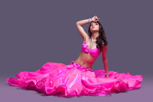 Full length portrait of beautiful dancer in pink costume sitting on floor