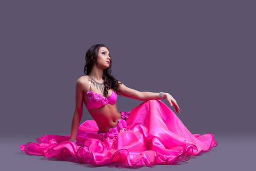Full length portrait of pretty woman - dancer in oriental pink costume sitting on floor